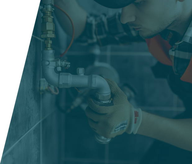 Plumber wearing gloves and a cap working on a metal pipe installation in a tiled bathroom.